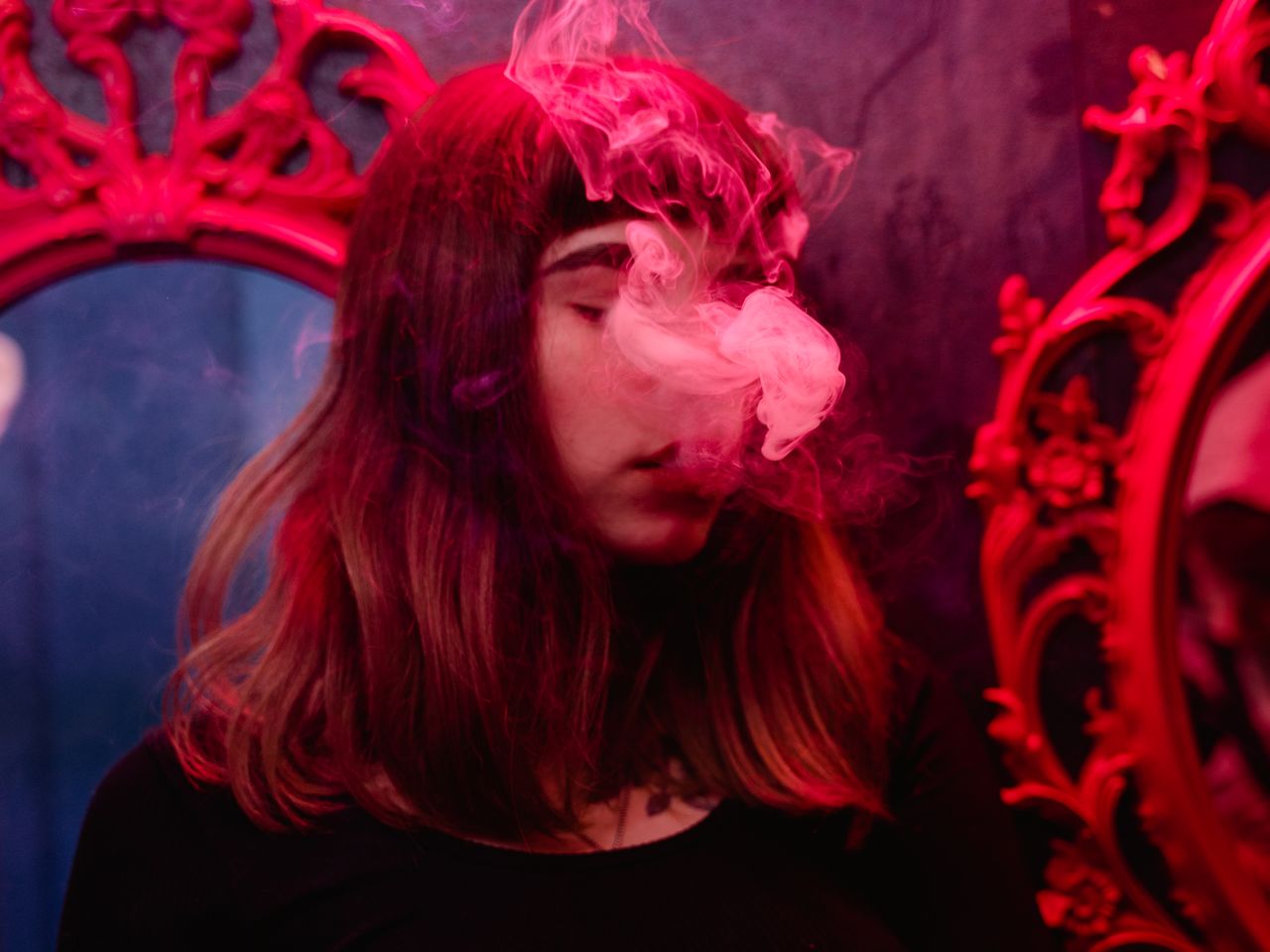 services-01 A woman enveloped in smoke with red lighting in a vintage room setting.