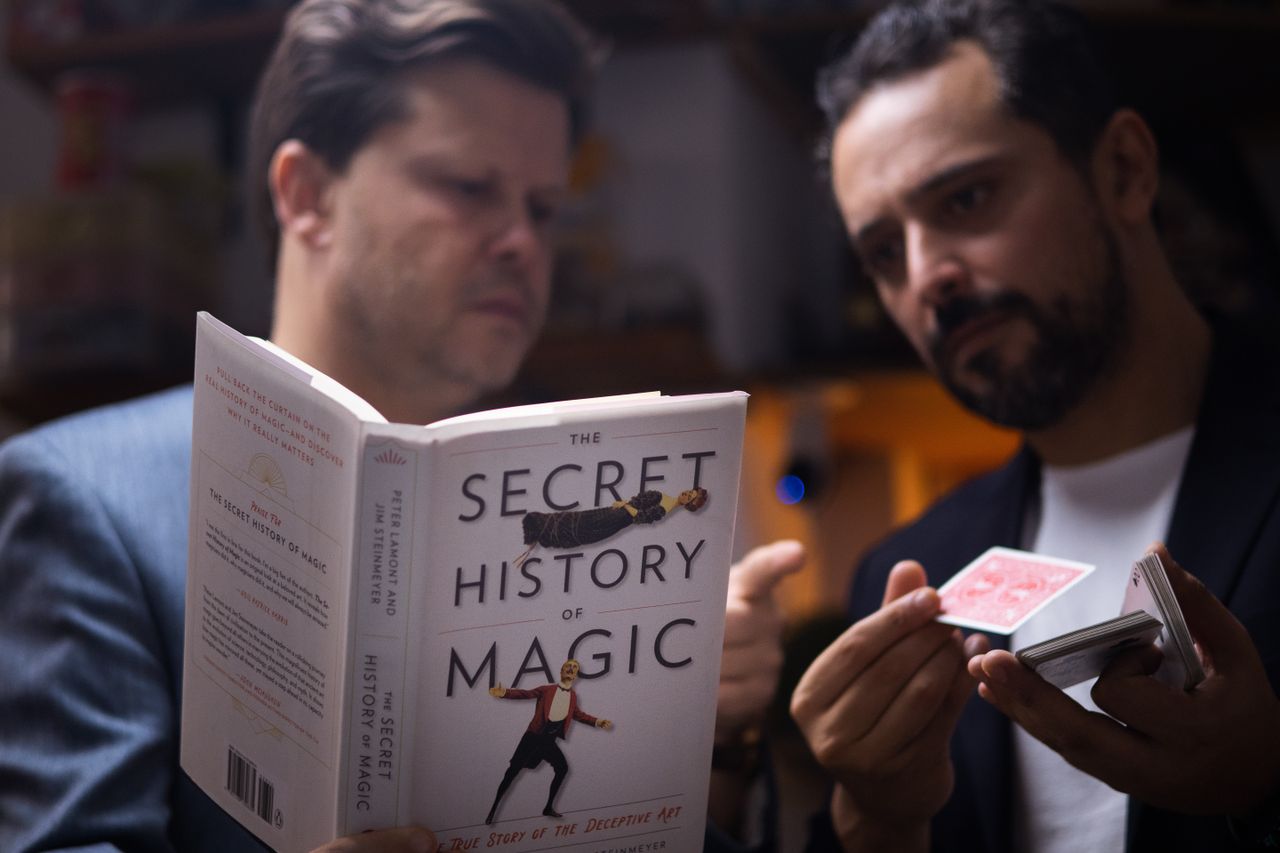 services-02 Two magicians focus on a magic book and playing cards, creating mystery.