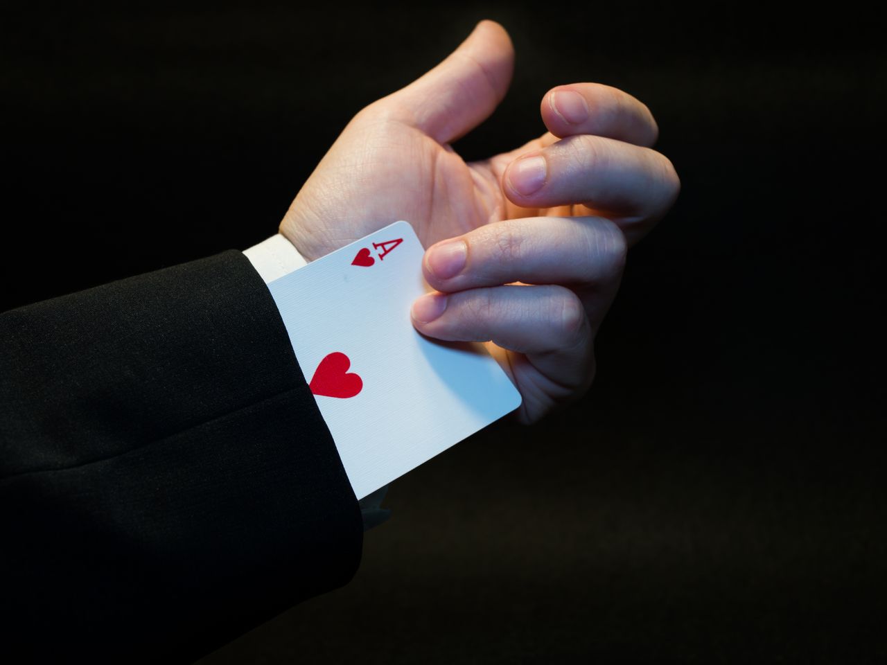 A magicians hand showing an ace of hearts hidden up the sleeve, symbolizing magic and trickery.